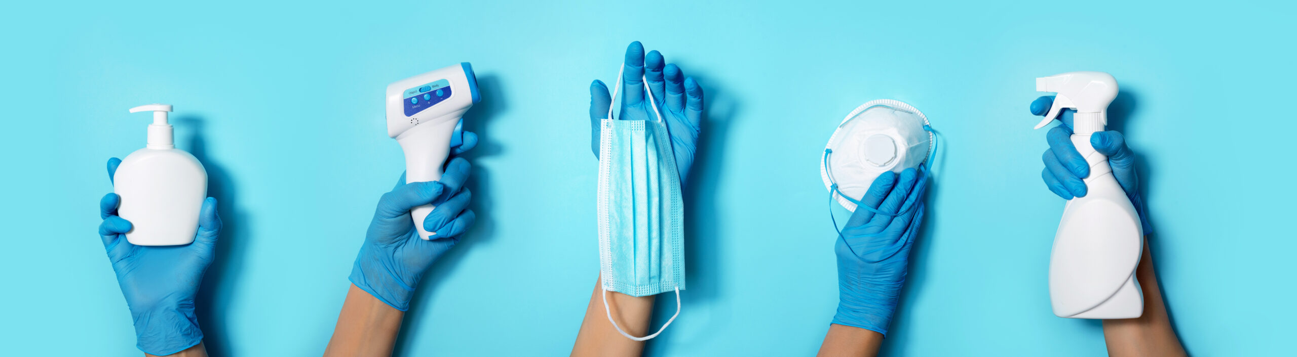 Raised hands in medical gloves holding masks, sanitizers, soap, non contact thermometer on blue background. Banner. Copy space. Health protection equipment during quarantine Coronavirus pandemic.